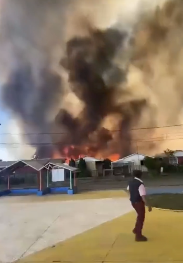 An official helps guide evacuees as a wildfire burns through houses in Chile.